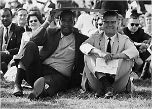file:/activities/oralhistory/cappics/romer1963_blackwhite, alt: two protesters--one black, one white, sharing the shade of a placard